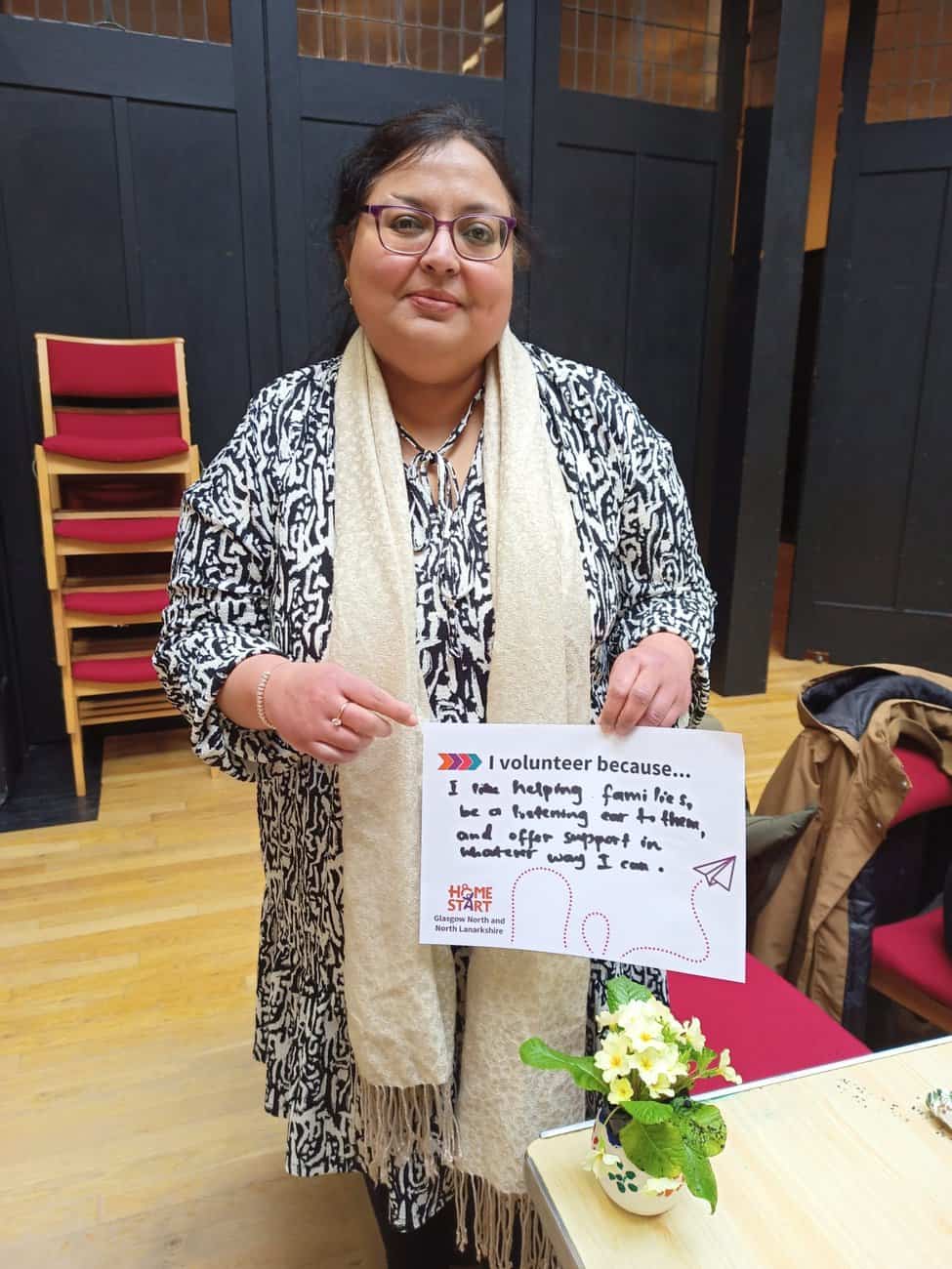 Image of Home-Start Volunteer holding a card saying I volunteer because I like helping families, be a listening ear to the, and offer support in whatever way I can.