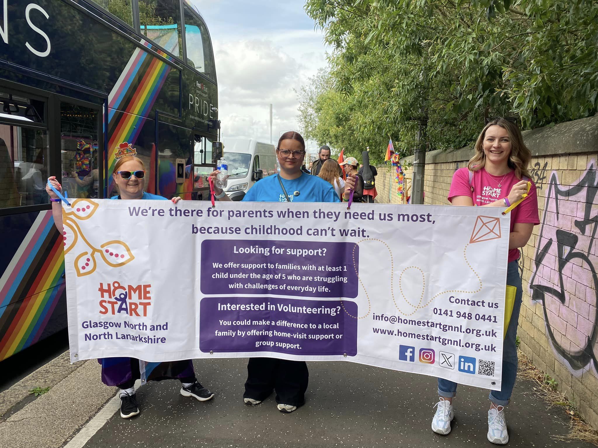 Image of Home-Start staff and friends holding a Home-Start banner walking at the Glasgow Pride March.