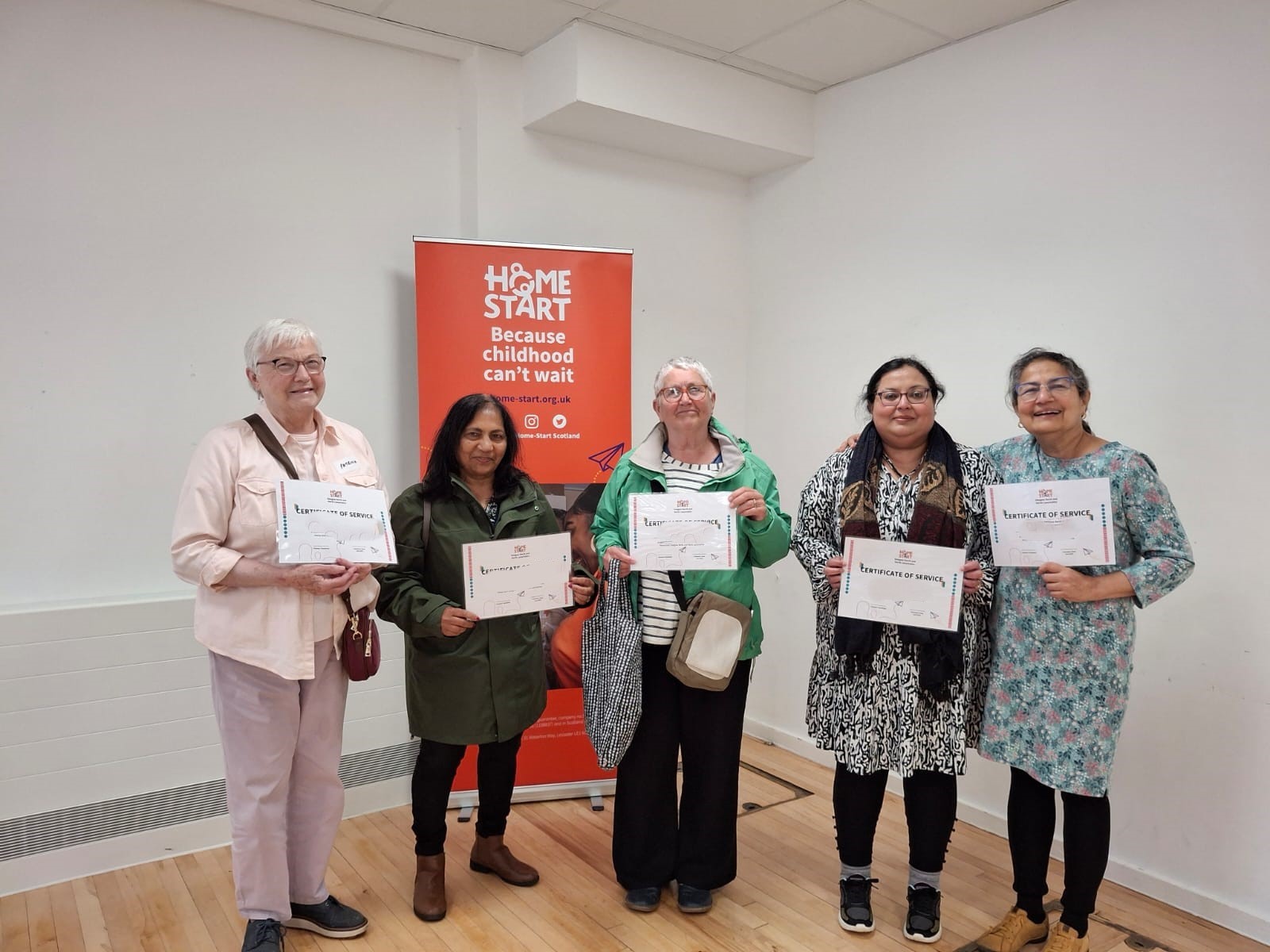 Image of 5 volunteers standing holding certificates for their service in supporting families.