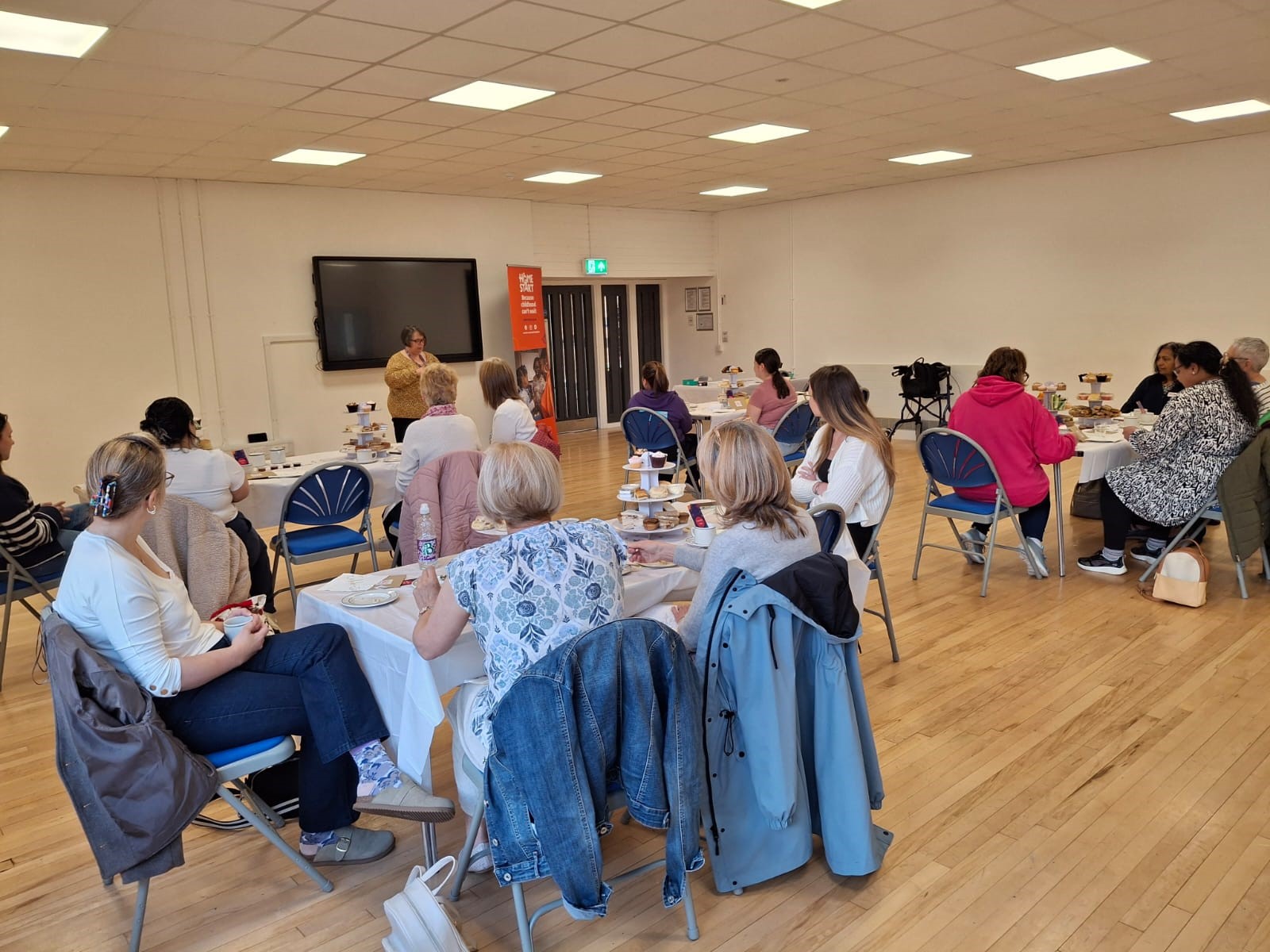 Image of volunteers in a hall sitting at tables eating an afternoon tea celebrating volunteers week.