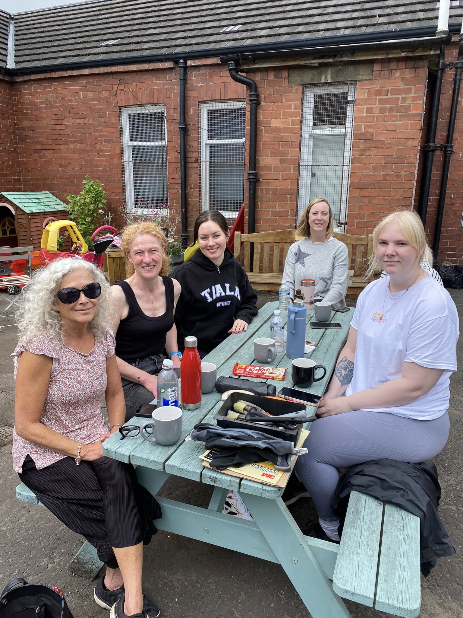 Image of Scullion Law team outside the Home-Start Hub sitting on the bench after tidying up the outdoor area.