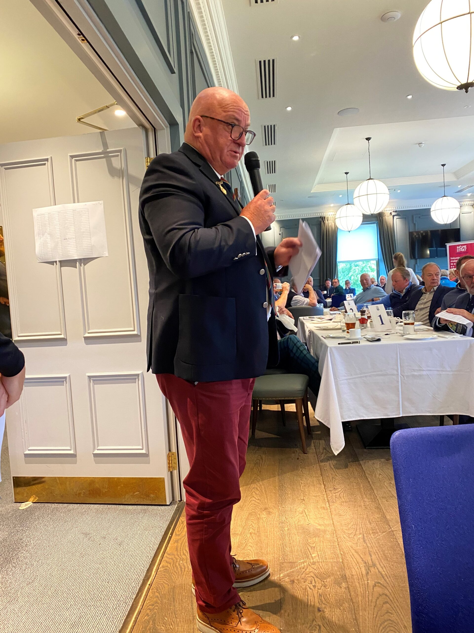 Image of man who is leading the auction at the charity event at the Glasgow Golf Club.  He standing with a microphone addressing everyone.