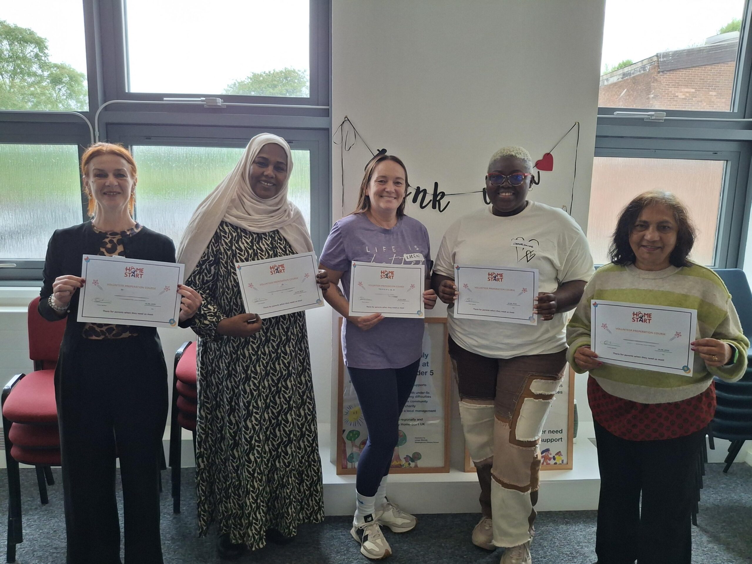 Image of 5 newly trained volunteers standing together and holding their certificates and smiling.