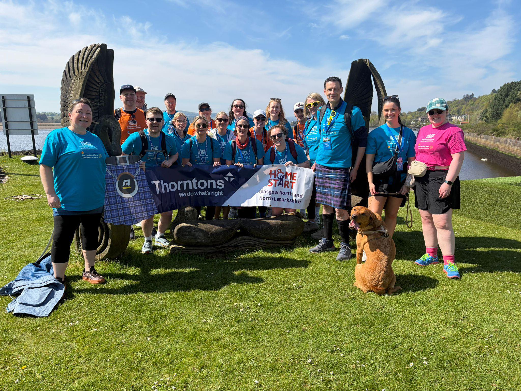 An image of the Thorntons Law after finishing the Kiltwalk, they are all standing on grass and and behind a banner with the Thorntons Logo and our Home-Start logo.