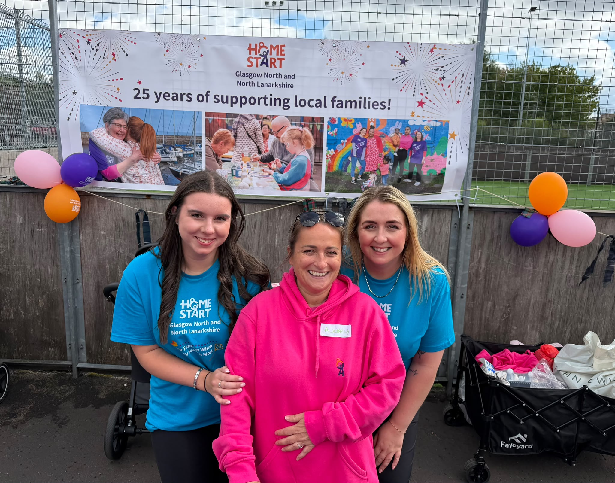 Image of our Family Engagement Coordinators standing smiling infront of our banner saying 25 years of supporting local famlies.